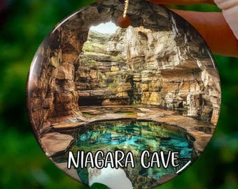 Puede incluir: Un adorno redondo de cerámica con una imagen de una cueva con una piscina de agua en su interior. El texto "NIAGARA CAVE" está impreso en el adorno.