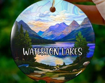 Könnte beinhalten: Ein runder Keramik-Anhänger mit einem Bild im Stil eines Buntglasfensters von einer Bergseenlandschaft. Der Text "WATERTON LAKES" ist in Weiß auf den Anhänger gedruckt.