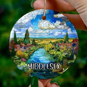 Puede incluir: Adorno navideño redondo de cerámica con una escena de paisaje con un río, casas y árboles bajo un cielo azul con nubes. La palabra "MIDDLESEX" está impresa en blanco. Se adjunta una cuerda dorada para colgar.