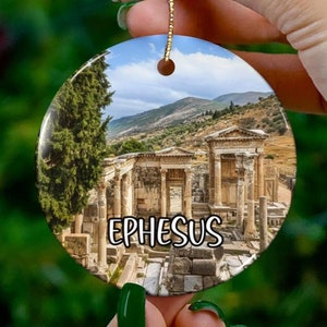 Puede incluir: Adorno de cerámica con una imagen colorida de las ruinas antiguas de Éfeso, Turquía. El adorno es redondo y tiene una cuerda dorada para colgar. El texto "EPHESUS" está impreso en el adorno.