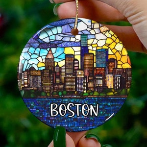 May include: A round, ceramic ornament with a stained glass design of the Boston skyline. The ornament is blue, green, yellow, and orange. The text "BOSTON" is printed in white on the ornament.