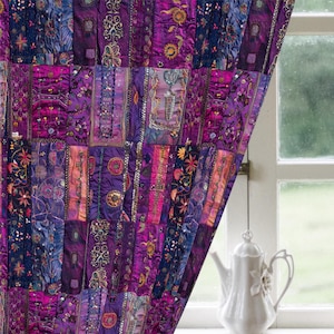 Puede incluir: Una cortina de patchwork en tonos morados, magenta y azul cuelga frente a una ventana. La cortina está hecha de piezas de tela rectangulares con detalles bordados y adornados. Una tetera blanca está en el alféizar.