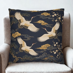 May include: A square throw pillow featuring a dark navy blue background with a repeating pattern of white and gold cranes in flight, stylized gold clouds, and delicate white cherry blossom branches with dark brown stems.