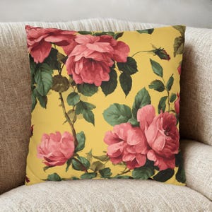 May include: Square throw pillow with a vibrant floral pattern. The pillow features large, pink roses with green leaves and stems against a yellow background. The design is reminiscent of vintage botanical prints.