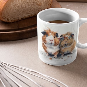 May include: White ceramic mug with a brown and white guinea pig wearing glasses and a brown and white guinea pig with a pink nose. The mug is filled with brown coffee.