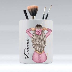 Könnte beinhalten: Weißer Keramik-Make-up-Pinselhalter mit einer rosa und weißen Illustration einer Frau mit langen blonden Haaren und einer rosa Schleife. Der Name "Emma" steht auf der Seite des Halters.