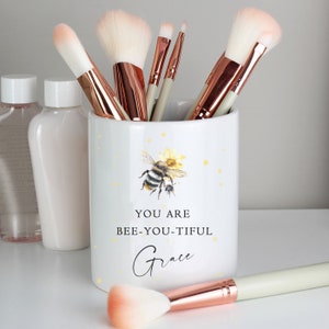 May include: White ceramic makeup brush holder with a bee and flower design. The holder has the text "You are bee-you-tiful Grace" printed on it.