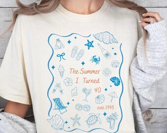May include: Cream-colored t-shirt with a blue illustrated design featuring beach-themed icons and the text "The Summer I Turned 40, est. 1995". The design includes seashells, a cocktail, and a beach chair.