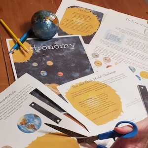Pode incluir: Um cartaz educativo colorido com a palavra "astronomia" em letras grandes e amarelas. O cartaz apresenta uma ilustração em aquarela de planetas e estrelas sobre um fundo azul escuro. Há também várias imagens menores de planetas, incluindo um close-up da Terra. O cartaz é acompanhado por um conjunto de instruções para um "Desafio de modelo do Sol e da Terra" que inclui uma fita métrica e um conjunto de planetas recortados.