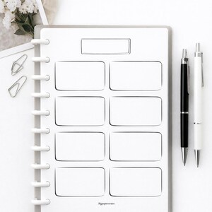 May include: A white planner with a rectangular design, featuring a series of boxes for notes. Two pens, one black and one white, are positioned to the right. The planner is bound with a white disc binding. The text "Mypapercraze" is visible.