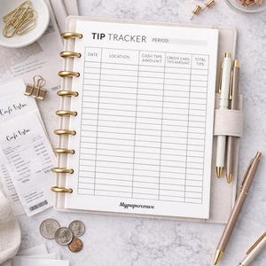 Pode incluir: Um caderno bege para rastreamento de gorjetas com detalhes dourados, canetas e material de escritório. O caderno tem um layout pautado para rastrear gorjetas, com o texto "TIP TRACKER" no topo. O caderno está aberto, revelando as páginas pautadas. O texto "Mypapercrave" está na parte inferior.