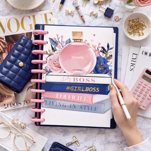May include: A flat lay featuring a pink planner with a perfume bottle illustration, books with text, and a navy blue wallet. Gold paper clips, pens, and a cup of coffee are also present. The planner has the text "Lady BOSS", "#GIRLBOSS", "L'OFFICIEL", and "LIVING IN STYLE".