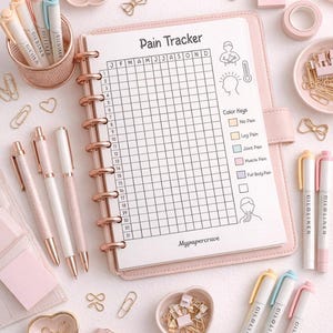 May include: Aesthetic flat lay featuring a pink pain tracker journal with a grid layout, color keys, and the text "Pain Tracker." The scene includes pens, paperclips, glasses, and other stationery items in shades of pink and gold.