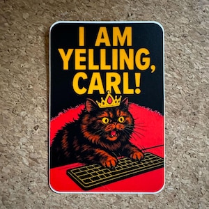 May include: A rectangular sticker with a black background and the text "I AM YELLING, CARL!" in yellow. A cartoon cat wearing a crown is in the center, with a keyboard below. The cat is black and orange.