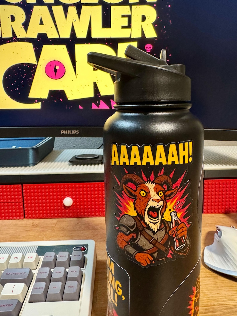 May include: Black water bottle with a black flip-top lid. The bottle features a sticker with a cartoon goat character yelling and holding a bottle. The text "AAAAAAH!" is above the goat.