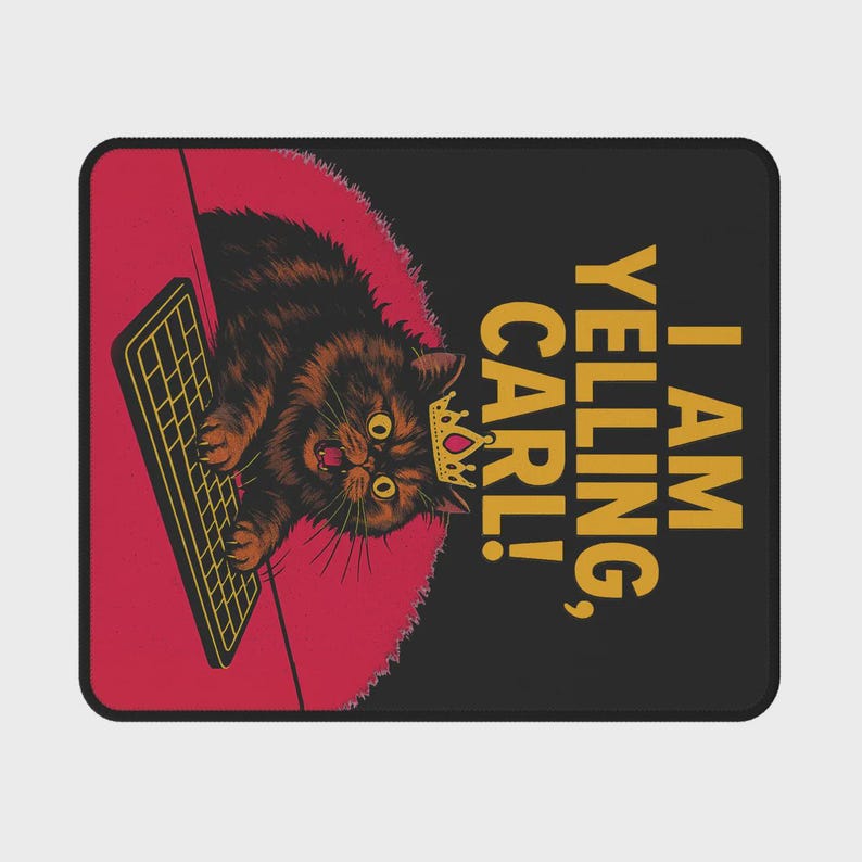 Op de afbeelding: Zwart rechthoekig mousepad met een cartoonkat met een kroon en schreeuwend naar een toetsenbord. De tekst "I AM YELLING, CARL!" is in goud gedrukt. De achtergrond is rood en zwart.