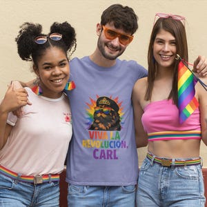 May include: A light purple t-shirt featuring a graphic of a cat wearing a crown and rainbow sunglasses, surrounded by a colourful sunburst. Below the cat, the text reads VIVA LA REVOLUCION, CARL in bold, multi-coloured capital letters.