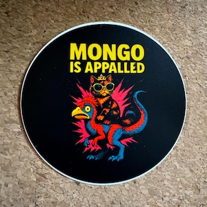 May include: A round sticker with a black background and a white border. The sticker features a cartoon cat wearing sunglasses and a crown, riding a colorful dinosaur. The text "MONGO IS APPALLED" is in yellow.