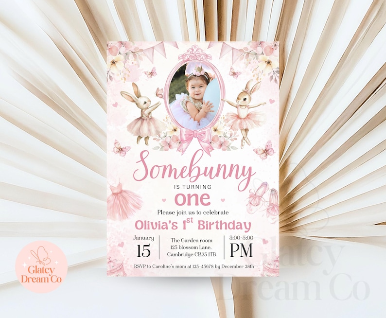 May include: Pink and white first birthday invitation featuring a bunny rabbit and a photo of a child in a pink dress. The invitation reads "Somebunny is turning one" and includes the date and time of the party.