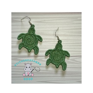Może przedstawiać: Para zielonych kolczyków w kształcie żółwia ze spiralnym wzorem. Kolczyki są wykonane z tkaniny i mają srebrne haczyki.