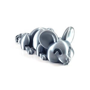 May include: A silver-colored 3D printed mouse figurine with a textured surface. The mouse is lying on its belly with its head turned to the side and its eyes closed.