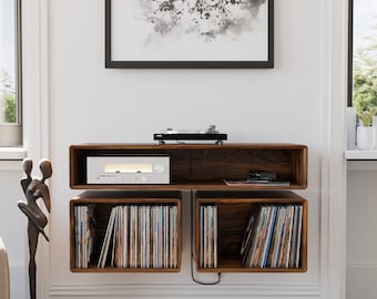 May include: A wall-mounted wooden record player shelf with three compartments. The top compartment has a turntable and a silver stereo receiver. The bottom two compartments are filled with vinyl records.