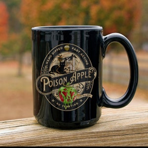 May include: Black ceramic mug with a graphic of a green apple with red dripping liquid. The graphic says "Poison Apple" with the text "Hand Dipped Fast Acting - Just One Bite - So Tempting" around the apple.