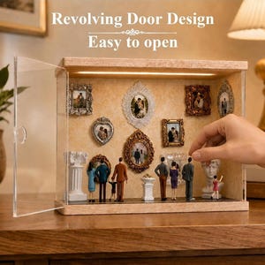 May include: A rectangular display case with a light wood frame and a clear acrylic revolving door. The interior features a beige textured back panel decorated with various ornate picture frames and miniature figurines of people and statues.