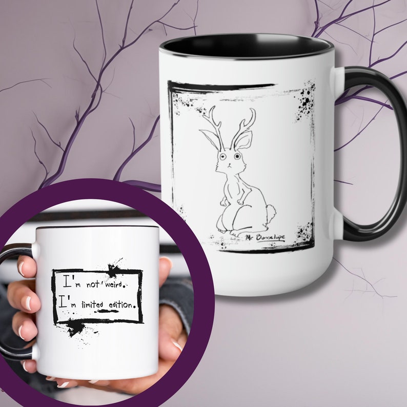 May include: White ceramic mug with a black rim and handle. The mug features a black and white illustration of a rabbit with antlers. The text "Mr. Dunlop" is written below the illustration. The mug has a black and white design with the text "I'm not weird. I'm limited edition."