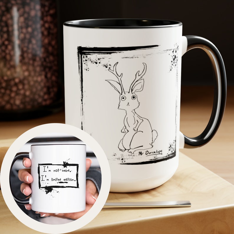 May include: White ceramic mug with a black rim and handle. The mug features a black and white illustration of a rabbit with antlers. The text "I'm not weird, I'm limited edition." is printed on the mug.