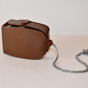 May include: A brown leather case with a silver chain and clip. The case has the word "Gossen" embossed on the front.