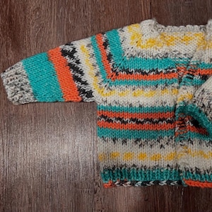 May include: A hand-knitted cardigan featuring a vibrant horizontal striped pattern in bright orange, turquoise, yellow, white, and speckled grey yarn. The garment has long sleeves, a round neckline, and a thick, textured knit construction throughout.