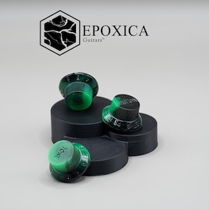 Può includere: Manopole per chitarra verdi e nere con numeri bianchi e la scritta "TONE" su una manopola. Le manopole sono esposte su una piattaforma nera a più livelli. Il logo "EPOXICA Guitars" è sullo sfondo.