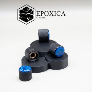 May include: A collection of black guitar knobs with blue resin tops. The knobs are arranged on a black platform. The brand name "EPOXICA Guitars" is displayed above the knobs.