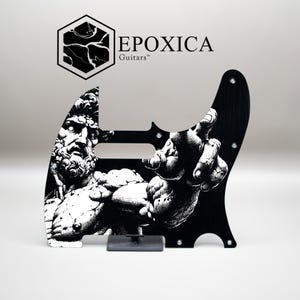 Puede incluir: Golpeador de guitarra negro con una ilustración en blanco y negro de una estatua clásica. El golpeador tiene el texto "EPOXICA Guitars" y está montado sobre un soporte transparente.