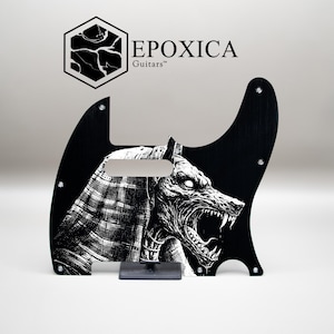 Puede incluir: Golpeador de guitarra negro con una ilustración detallada en blanco y negro de un lobo gruñendo. El golpeador tiene una forma única e incluye el texto "EPOXICA Guitars" y un logotipo.