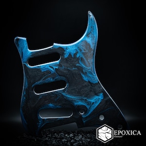 May include: A guitar pickguard featuring a marbled pattern of deep black and vibrant electric blue swirls. The component includes three elongated cutouts for pickups and several circular mounting holes. The text EPOXICA Guitars is visible.
