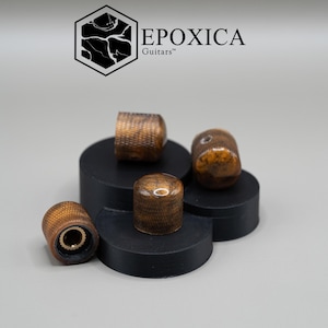 May include: Four cylindrical guitar control knobs with a polished amber-toned wood grain finish and textured sides. Each knob features a metallic interior insert. The text EPOXICA Guitars is displayed above the knobs with a hexagonal logo.
