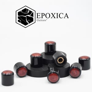 Peut inclure: Boutons de guitare noirs avec un motif marbré rouge et marron. Les boutons sont cylindriques avec un dessus plat et sont disposés sur une surface blanche. La marque "EPOXICA Guitars" est affichée au-dessus.