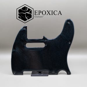 May include: A black guitar pickguard with a subtle swirling marble-like texture and a glossy finish. The piece features several pre-drilled screw holes and a cutout for a pickup. Above the pickguard, the text EPOXICA Guitars is visible.