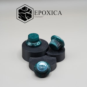 May include: Four teal guitar knobs, one labelled "TONE", on black platforms. The logo "EPOXICA Guitars" is in the upper left corner. The knobs have a metallic finish. The knobs are for guitars.