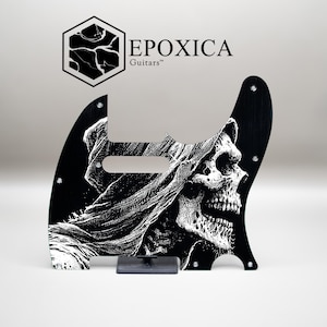 May include: Black guitar pickguard with a white illustration of a skull in a hooded cloak. The pickguard has a distinctive shape and features the text "EPOXICA Guitars" and a logo.