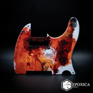 May include: A guitar pickguard featuring an abstract, fluid design with vibrant shades of orange, deep red, black, and white. The surface displays swirling, ink-like patterns and textures. The logo for Epoxica Guitars is visible in the bottom corner.
