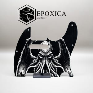 Peut inclure: Pickguard de guitare noir avec une illustration blanche détaillée d'une créature tentaculaire ailée. Le pickguard a une forme unique et comprend le texte "EPOXICA Guitars" et un logo.