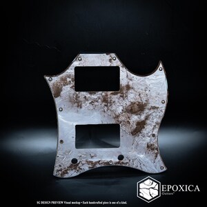 May include: A guitar pickguard with a marbled pattern in shades of white, silver, and dark brown. The piece features two rectangular cutouts for pickups and several small screw holes. Text at the bottom reads SG DESIGN PREVIEW and EPOXICA Guitars.