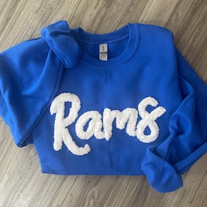 May include: A royal blue sweatshirt with a white fluffy applique of the word "Rams".