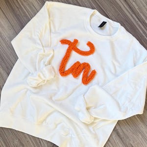 May include: White sweatshirt with a large orange fluffy "I'm" design.