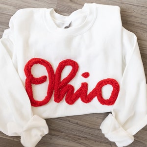 May include: White sweatshirt with a red fuzzy applique of the word "Ohio".