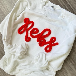 May include: White sweatshirt with a red fuzzy applique that says "Reba".