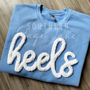 May include: Light blue sweatshirt with the word "Heels" in white fluffy letters.